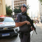 Policial militar armado próximo a viatura no Centro de São Paulo.